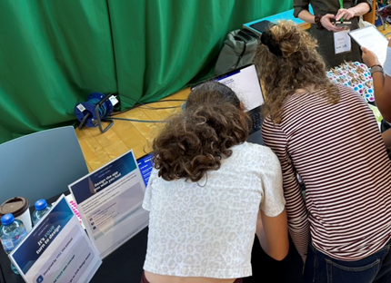 Young people at the booth laptop with the “Design the app you wish you had” table signs.