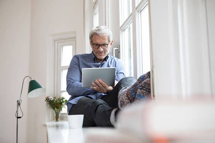 mature man sitting at window using tablet