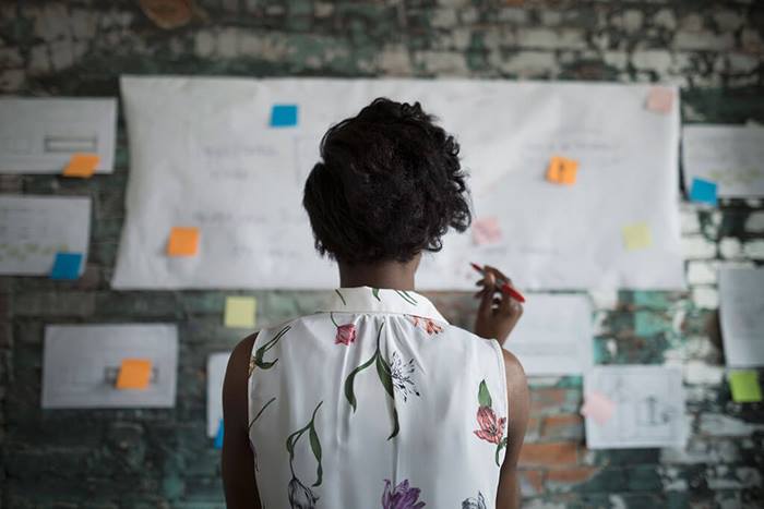 businesswoman reviewing flow chart hanging on brick wall in office