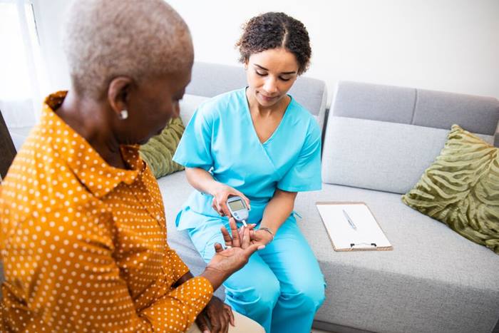 Nurse doing a glucose blood test on senior patient during home visit