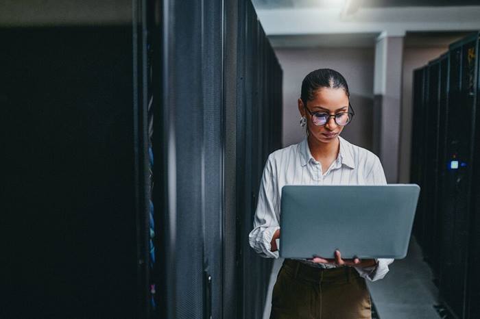 Young woman using laptop in server room