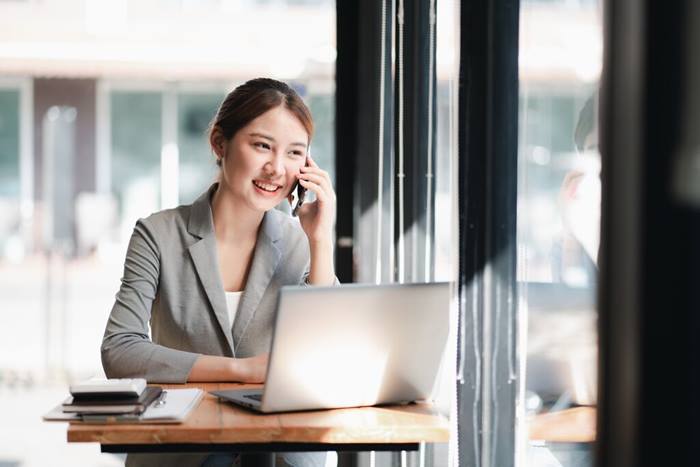 Woman talk on smartphone using laption in home office