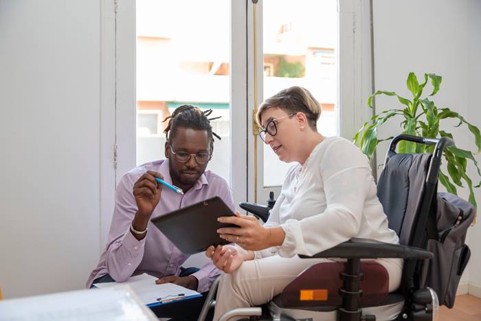 Business woman in a wheelchair looking at digital tablet with business partner