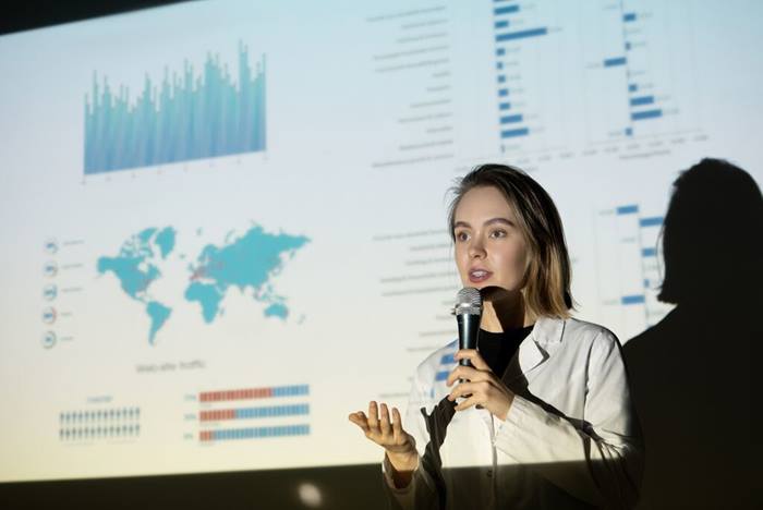 Woman in lab coat speaking into microphone during presentation